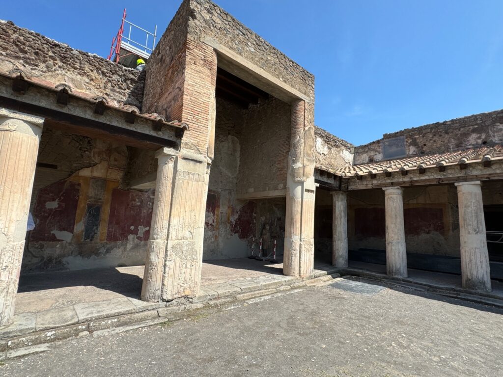 Ancient Roman ruins at Pompeii showing a courtyard with columns, weathered walls, and preserved architectural structures under clear blue sky