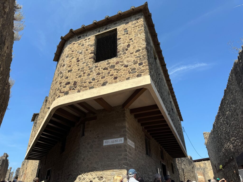 Historic stone tower with wooden reinforcements stands against clear blue sky in medieval village setting