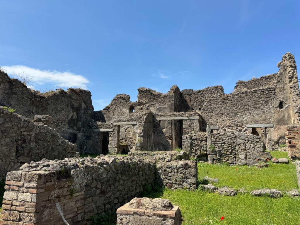 Ancient Roman ruins with stone walls and doorways stand amid green grass under a clear blue sky