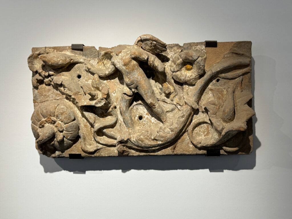 Carved stone relief depicting intertwined mythological creatures and decorative elements against a neutral museum wall