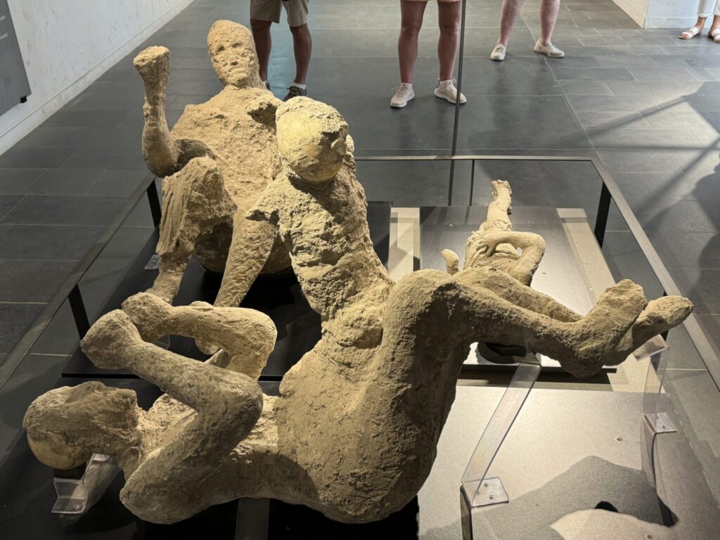 Ancient stone sculptures of intertwined human figures displayed in a museum gallery with visitors viewing in the background
