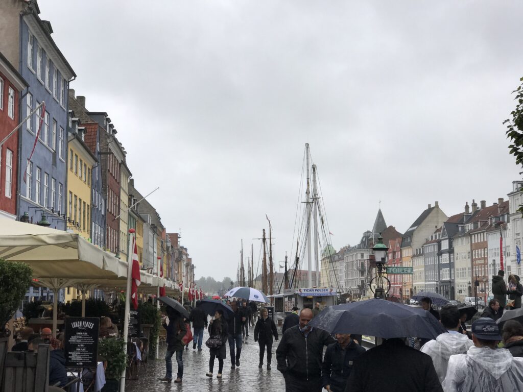 People walking along Nyhavn waterfront in Copenhagen with colorful buildings and umbrellas on a rainy day
