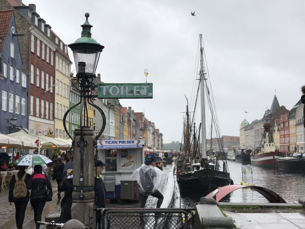 Rainy view of Nyhavn canal in Copenhagen with colorful buildings, boats, and people walking with umbrellas