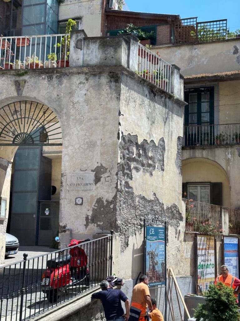 Weathered multi-story Italian building with peeling plaster, metal railings, and arched doorways in a narrow street