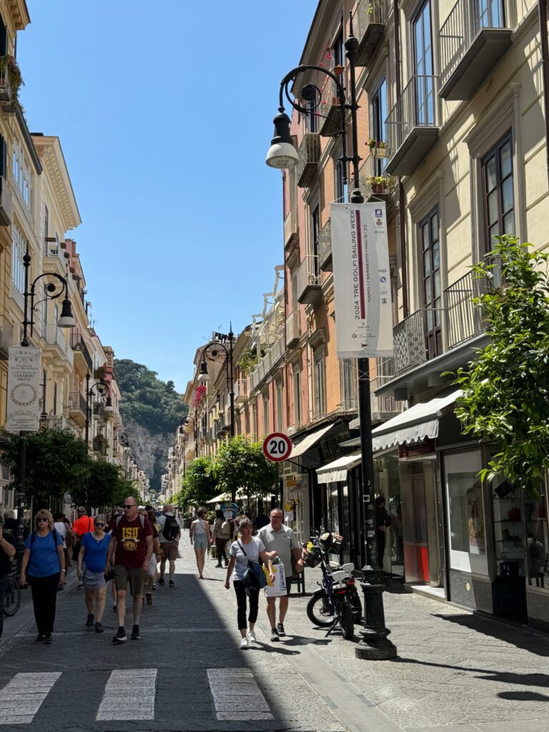 Pedestrian shopping street lined with historic buildings, shops, and cafes under clear blue sky in a European city