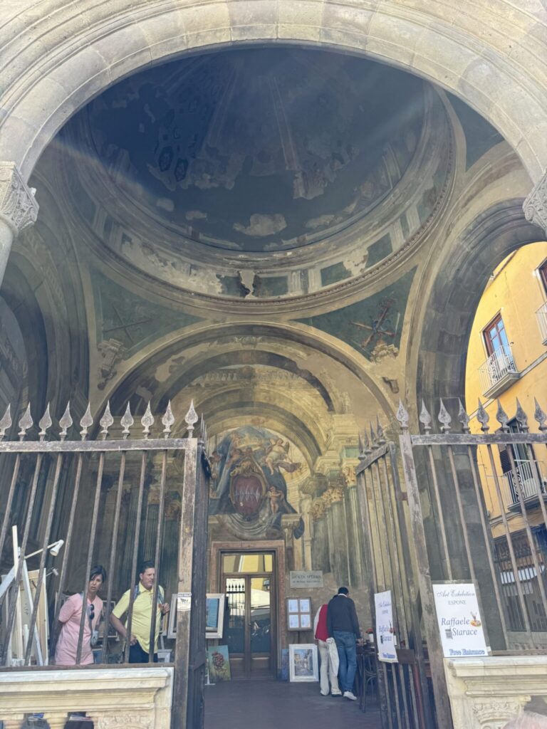 Ornate covered archway with barrel vault ceiling, classical columns, and religious frescoes in an Italian Renaissance-style courtyard or gallery