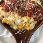 Baked pasta topped with melted mozzarella, marinara sauce, grated cheese, and parsley, served in a brown oval dish.
