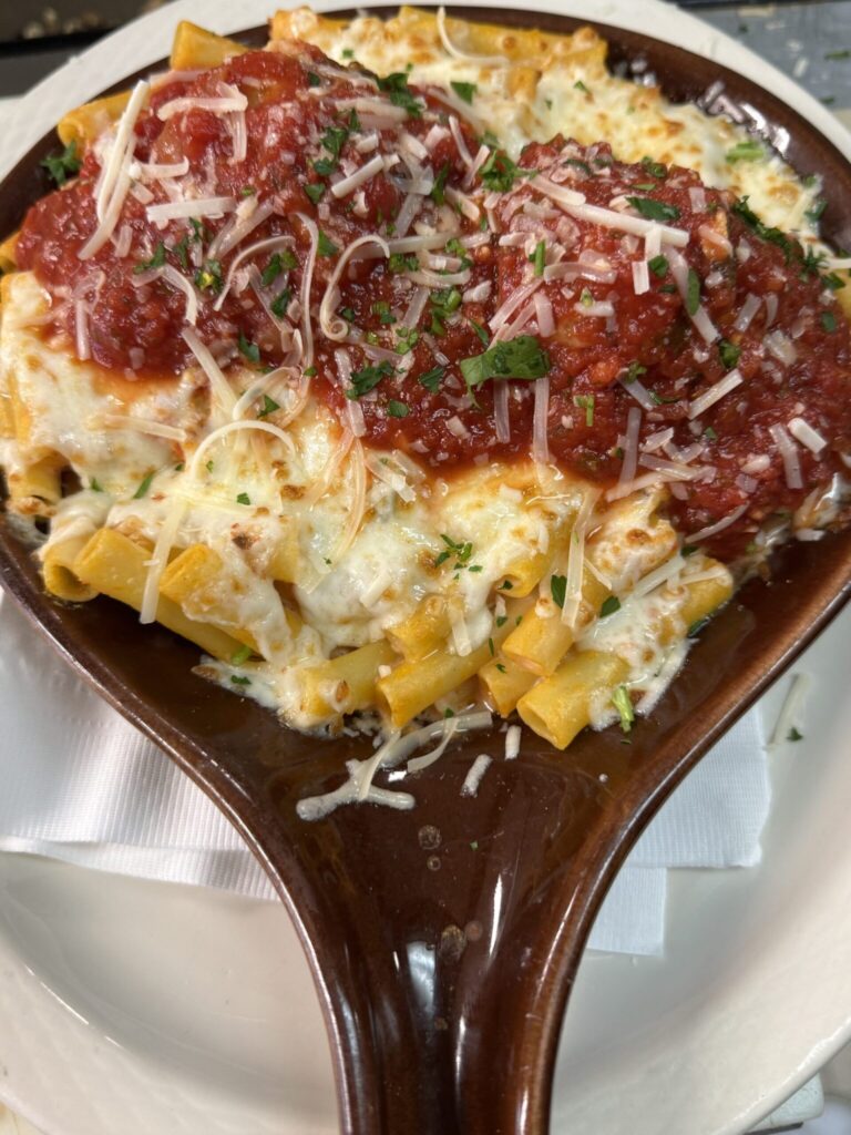 Baked pasta topped with melted mozzarella, marinara sauce, grated cheese, and parsley, served in a brown oval dish.