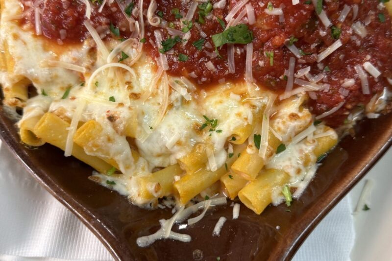 Baked pasta topped with melted mozzarella, marinara sauce, grated cheese, and parsley, served in a brown oval dish.