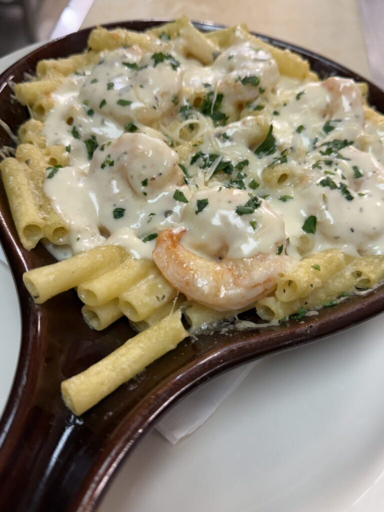 Rigatoni pasta with shrimp in a creamy white sauce, garnished with parsley, served in a brown oval dish.