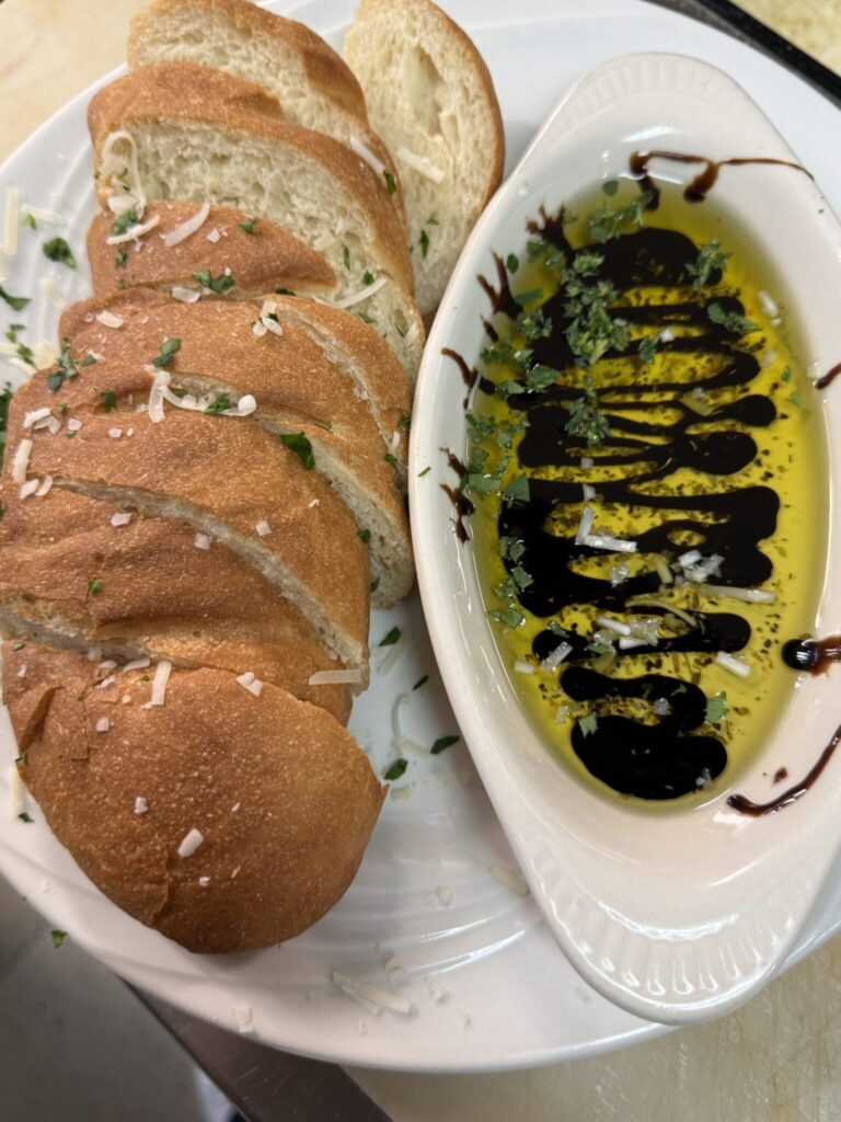 Sliced crusty bread served with olive oil and balsamic vinegar dip, topped with herbs and grated cheese.