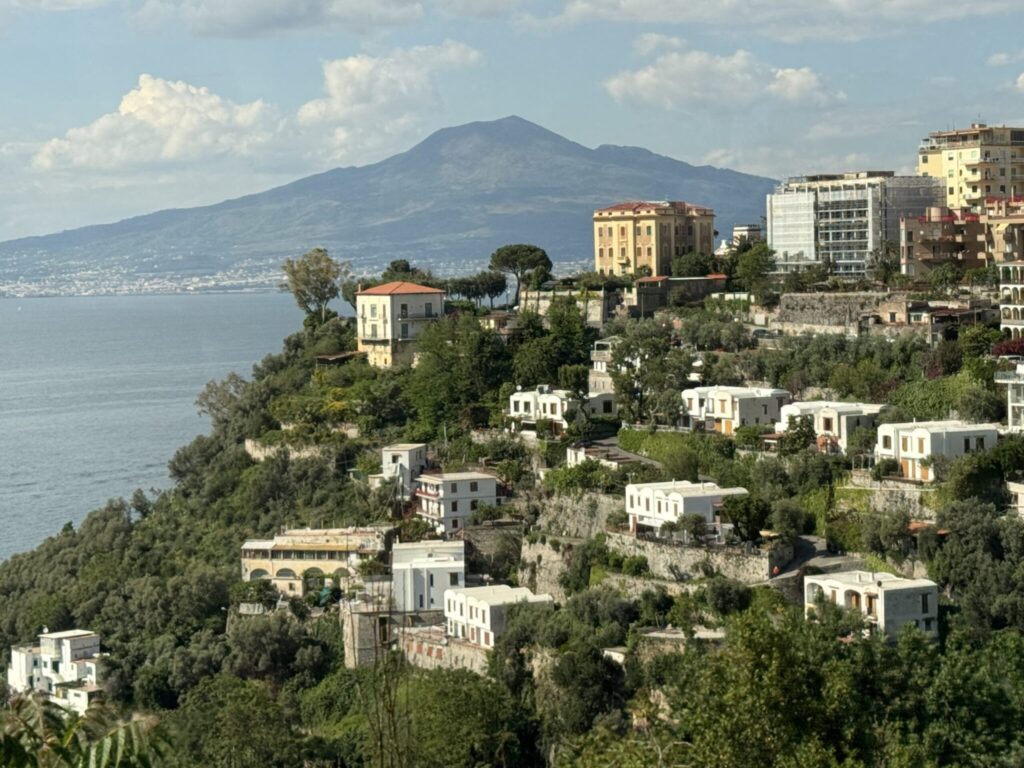 Coastal Italian town built on cliffsides overlooking the sea with Mount Vesuvius visible in the distant background