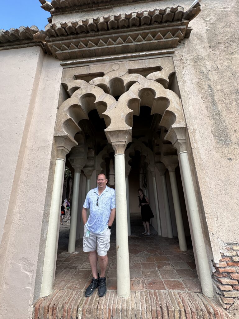 Man standing in ornate Moorish archway with horseshoe arch and decorative columns in historical building