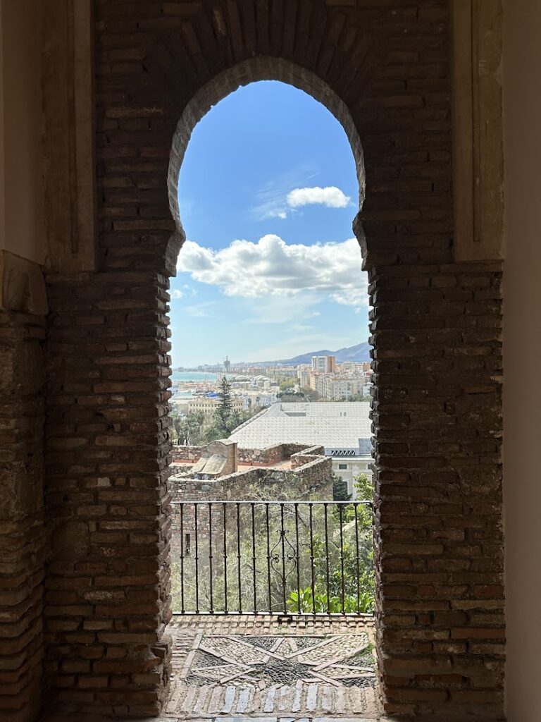 View through a Moorish arch of a Mediterranean coastal city with mountains and sea in the distance