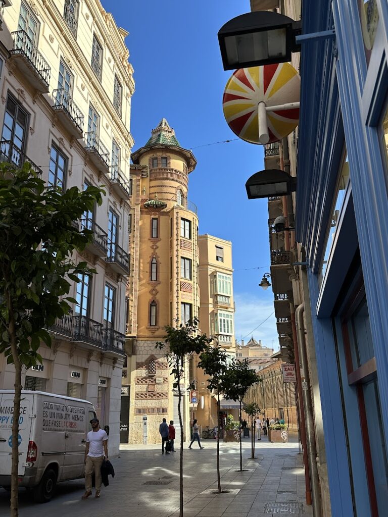 Narrow European street with historic architecture, ornate tower building, and decorative street lamp against blue sky