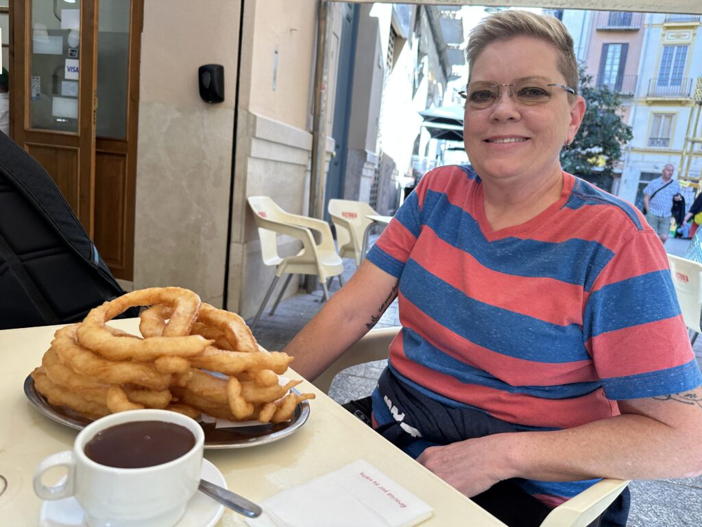 Woman in striped shirt smiles while posing with churros and chocolate sauce at a café table