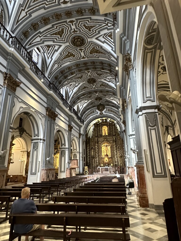 Interior of a grand cathedral with ornate vaulted ceilings, columns, wooden pews, and an illuminated altar at the far end