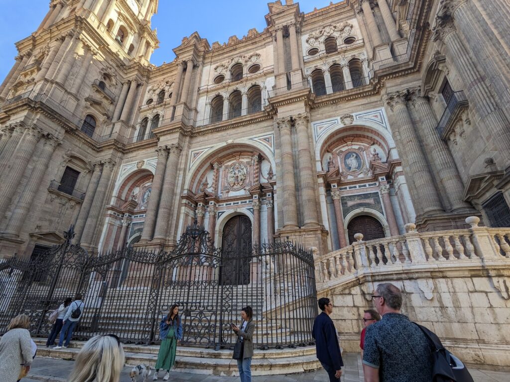 Ornate Renaissance cathedral facade with tall columns, arched doorways, and decorative reliefs, with tourists gathered in the plaza below