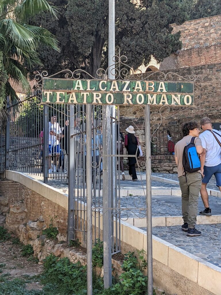 Ornate metal gate with "Alcazaba Teatro Romano" sign at ancient Roman theater ruins in Spain