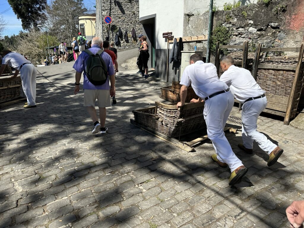Carreiros do Monte drivers pushing wicker toboggan sled down cobblestone street in Madeira