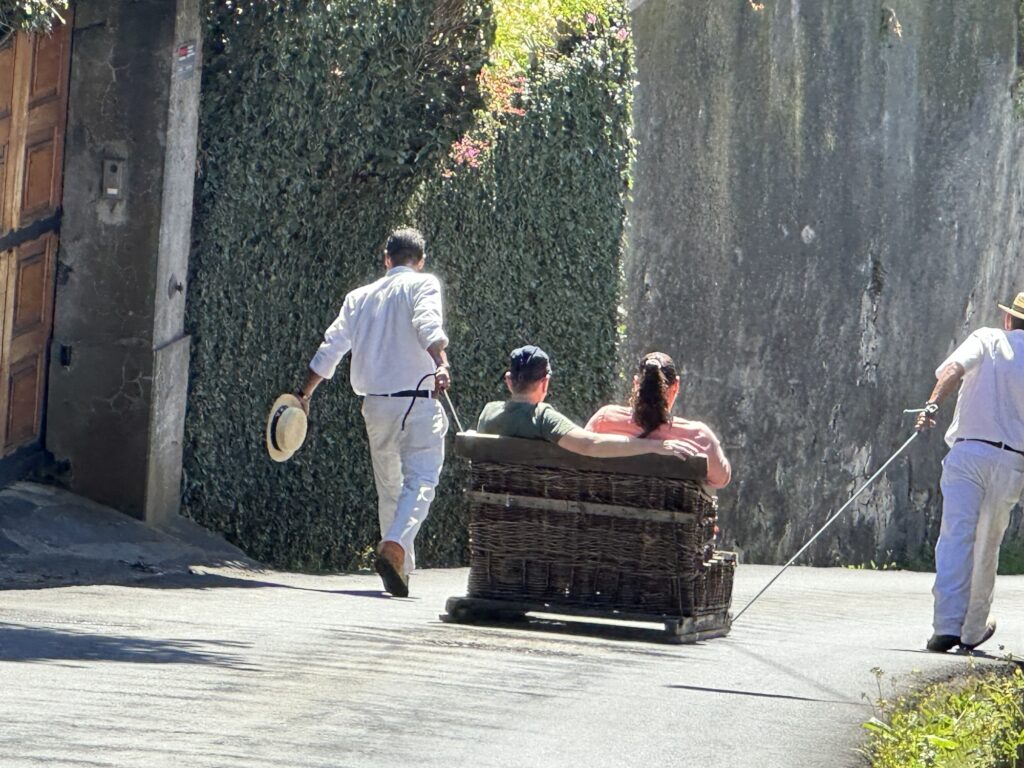 Couple riding Madeira toboggan sled guided by Carreiros down a steep street in Monte