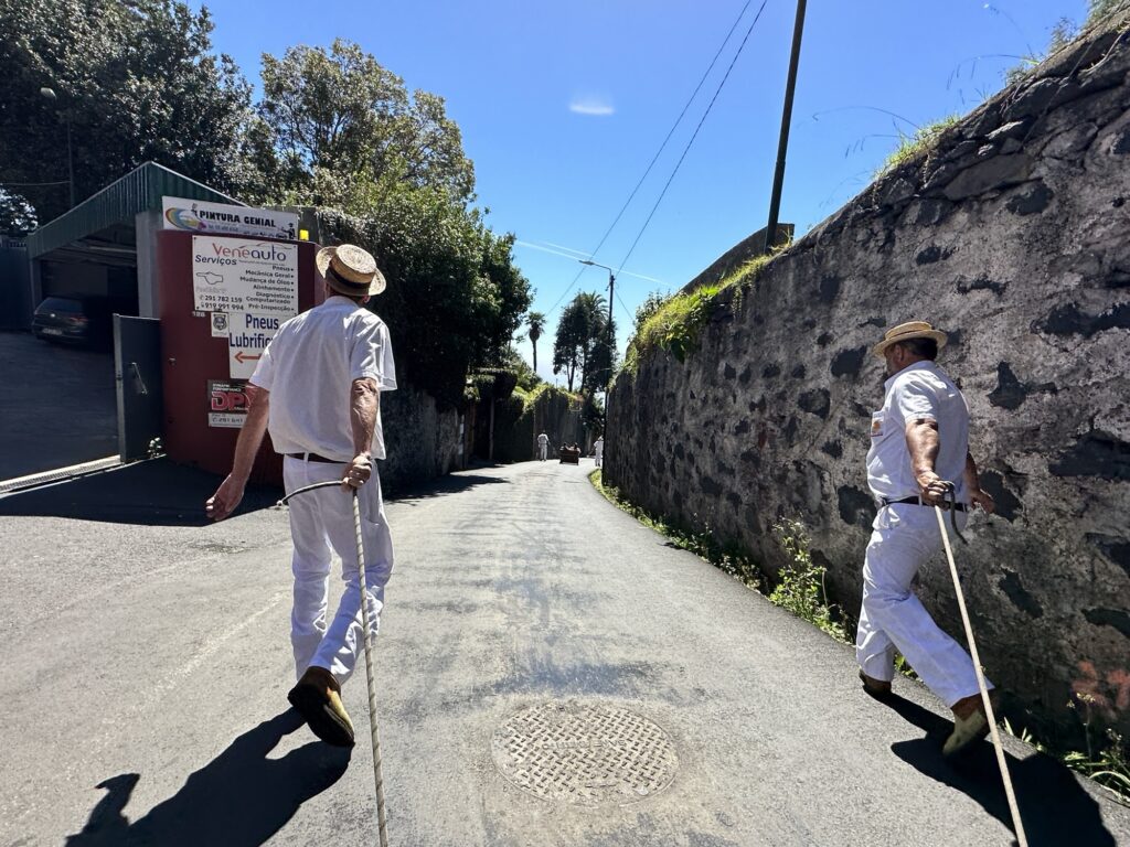 Carreiros do Monte drivers walking uphill with ropes after completing toboggan ride in Madeira