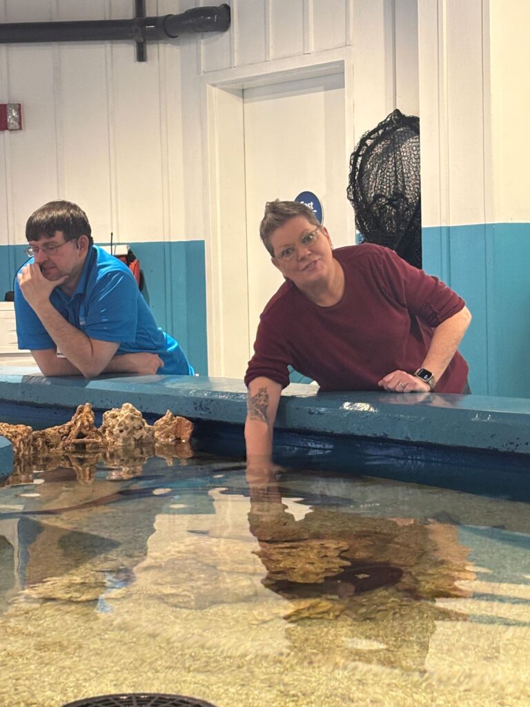 Two people observe marine life in a shallow tank at an aquarium or educational facility