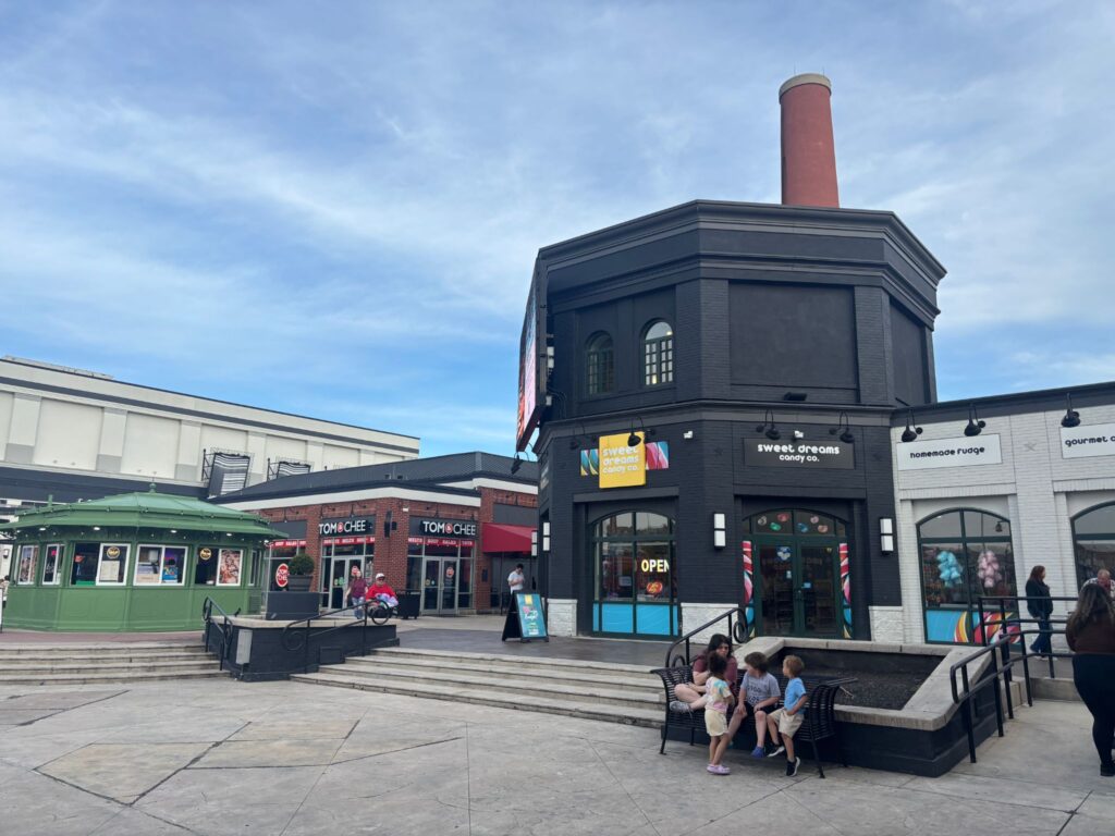 A distinctive black octagonal building with a red chimney sits in a pedestrian plaza surrounded by colorful storefronts and visitors