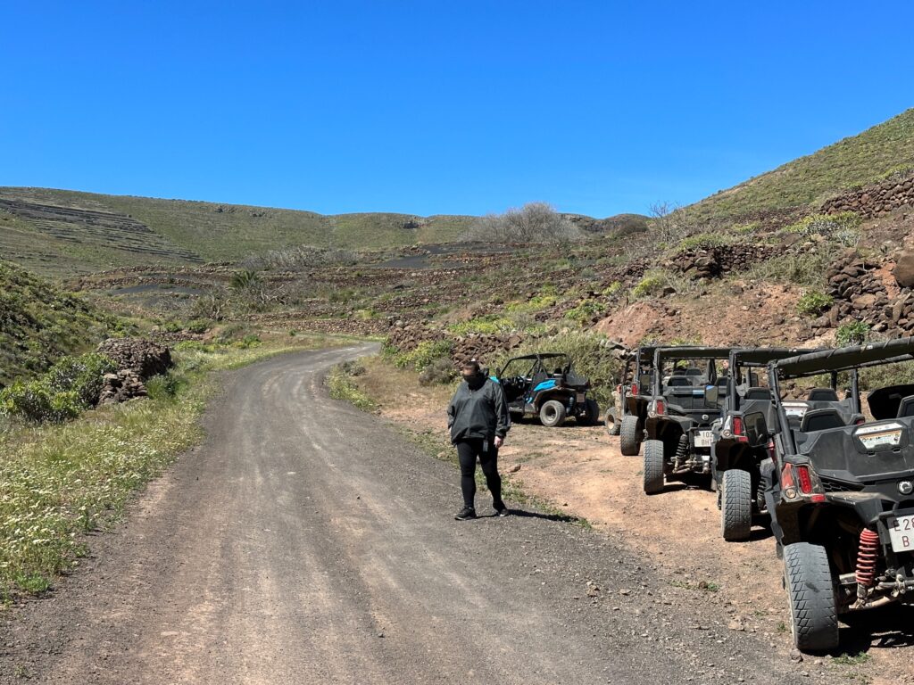 Off-road vehicles parked at a dirt trailhead in a rocky, arid hillside landscape with sparse vegetation