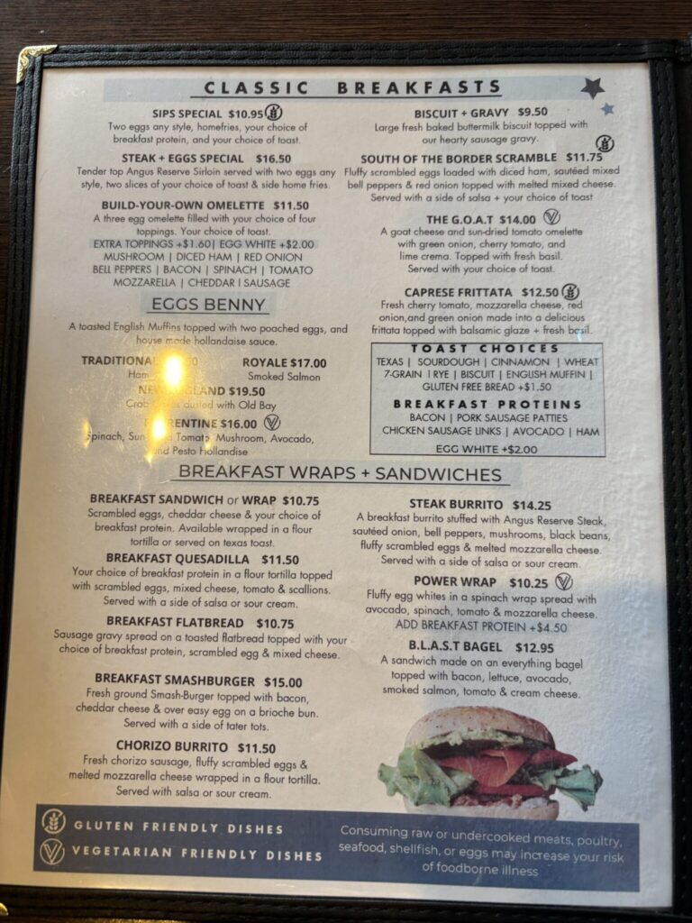 A menu board displaying classic breakfast options, wraps, sandwiches, and protein choices with prices ranging from $9.50 to $19.50