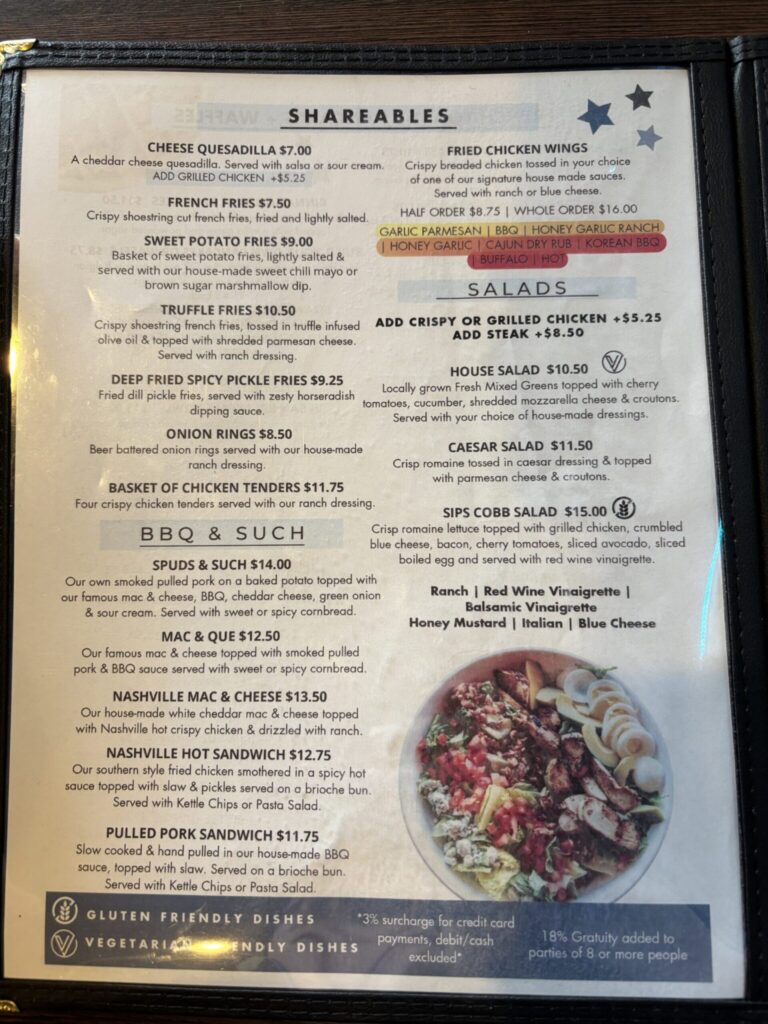 Restaurant menu displaying shareables, salads, BBQ dishes, and sandwiches with prices and descriptions on a wooden-framed board