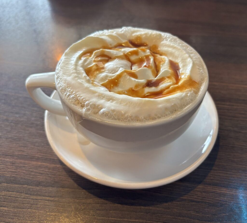 Chai latte with caramel drizzle and latte art foam in a white cup on a wooden table