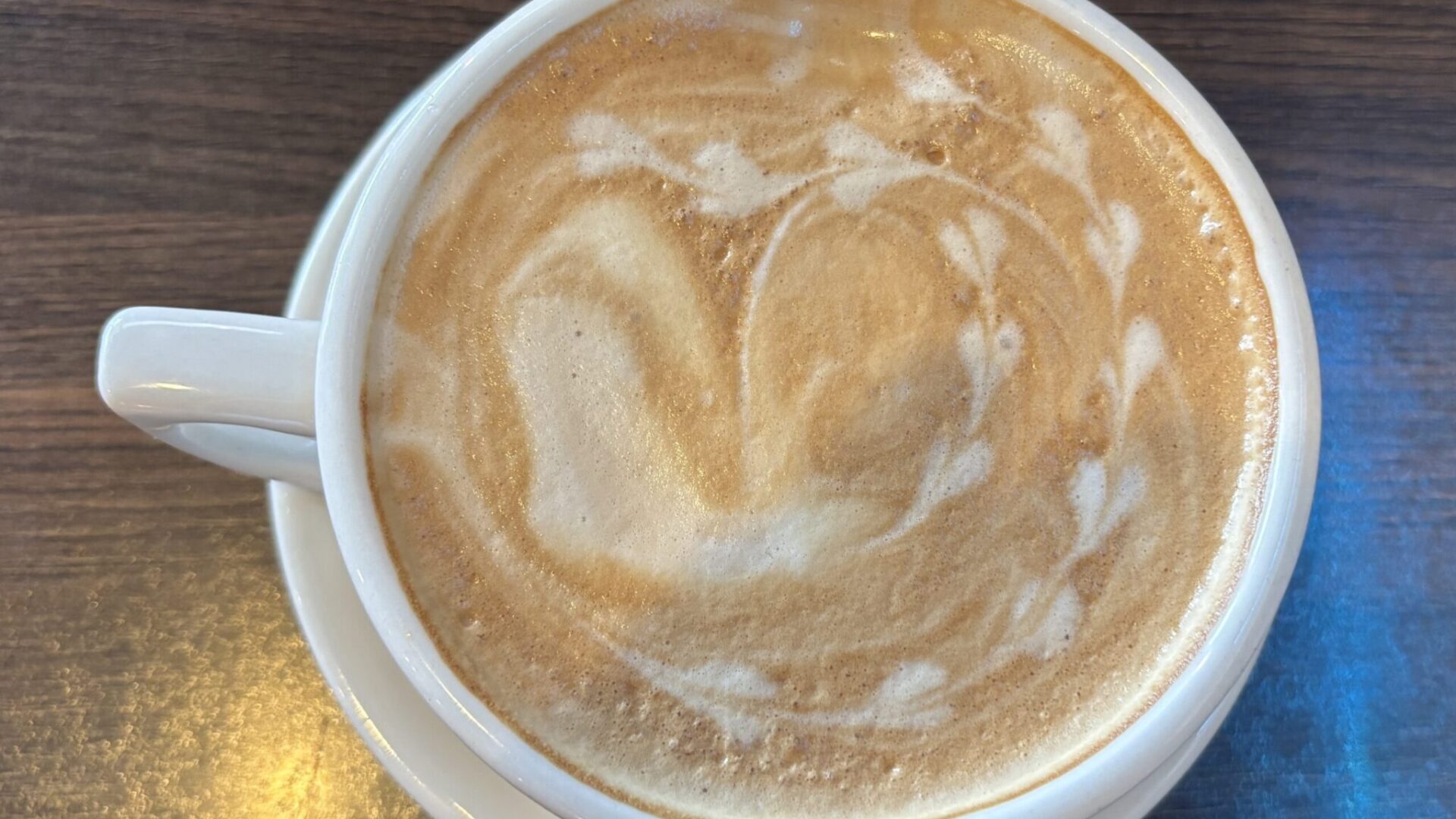 White ceramic mug of latte with latte art on a wooden surface