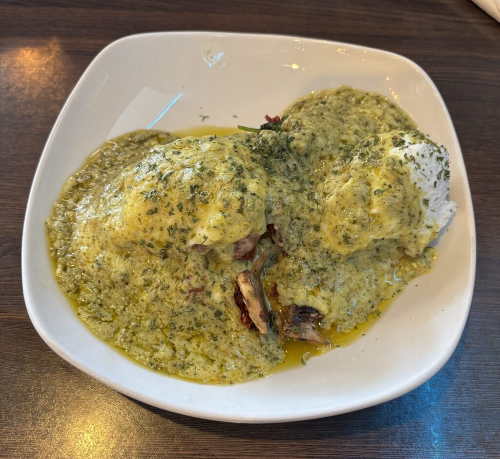 Eggs Benny Florentine served in a white bowl with green pesto sauce on a dark wooden table