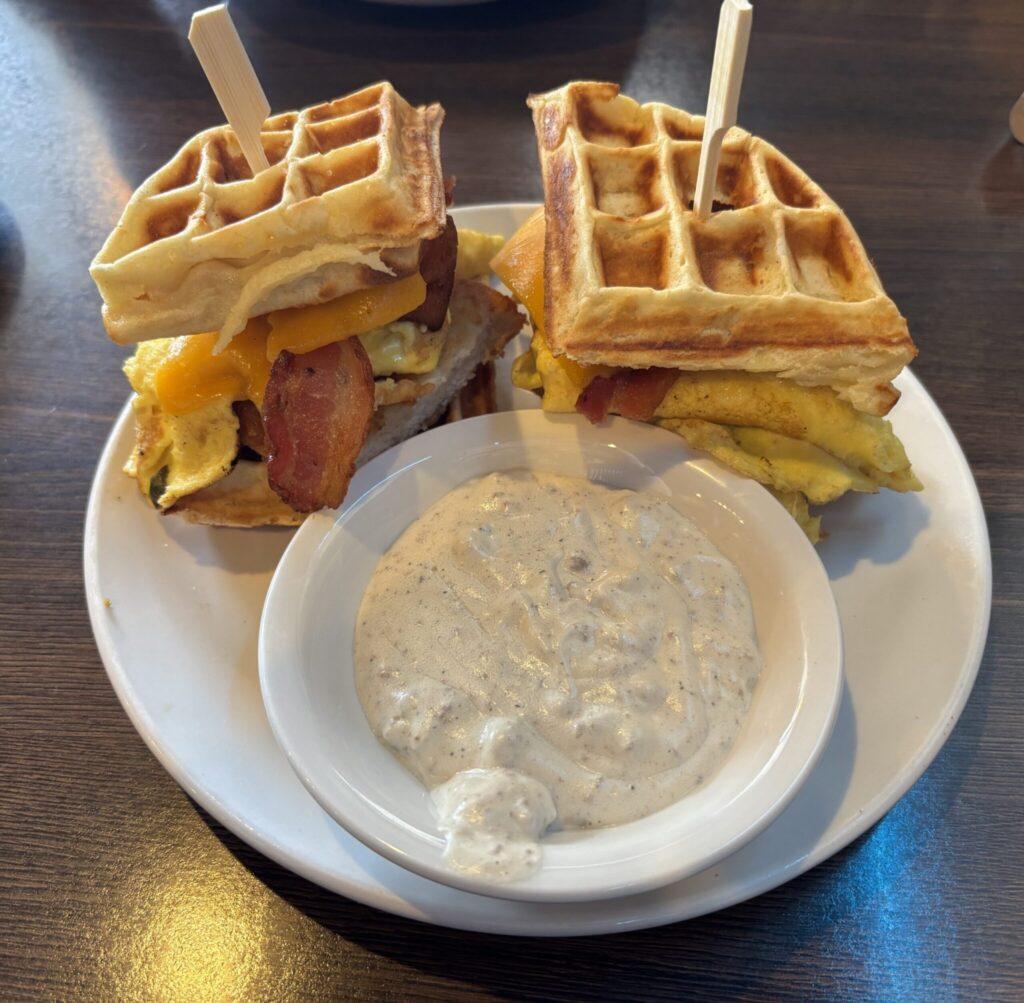 Two waffle sandwiches with egg and bacon served with a creamy sausage gravy dipping sauce on a white plate
