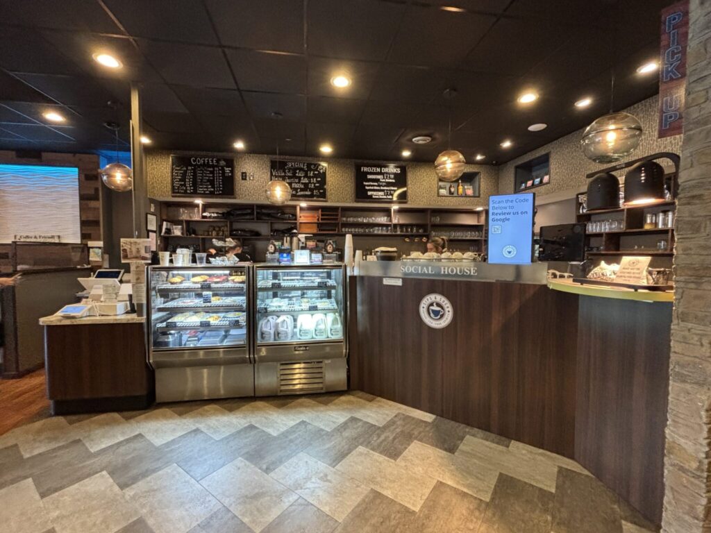 Modern coffee shop interior featuring counter with display cases, menu boards, and warm lighting in a casual café setting