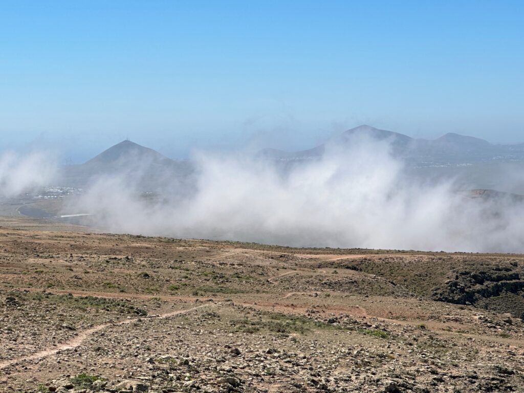 Fog blankets volcanic mountains and valleys in an arid, rocky landscape under clear blue sky
