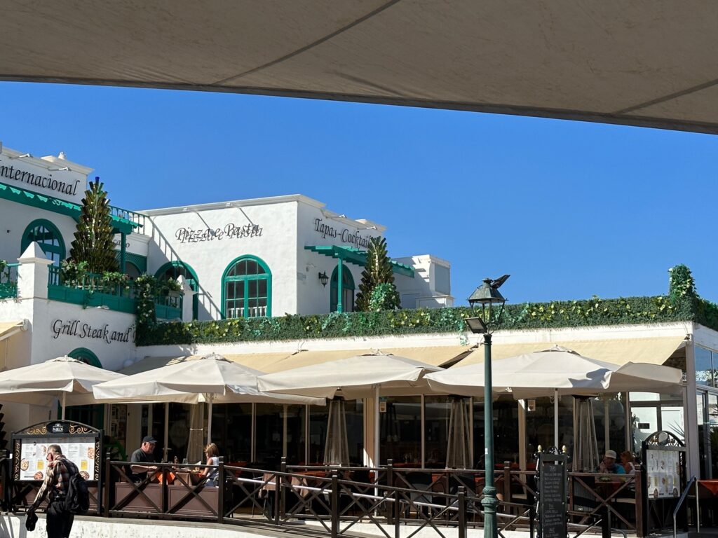 Beachfront restaurant with white umbrellas and green-trimmed building under clear blue sky
