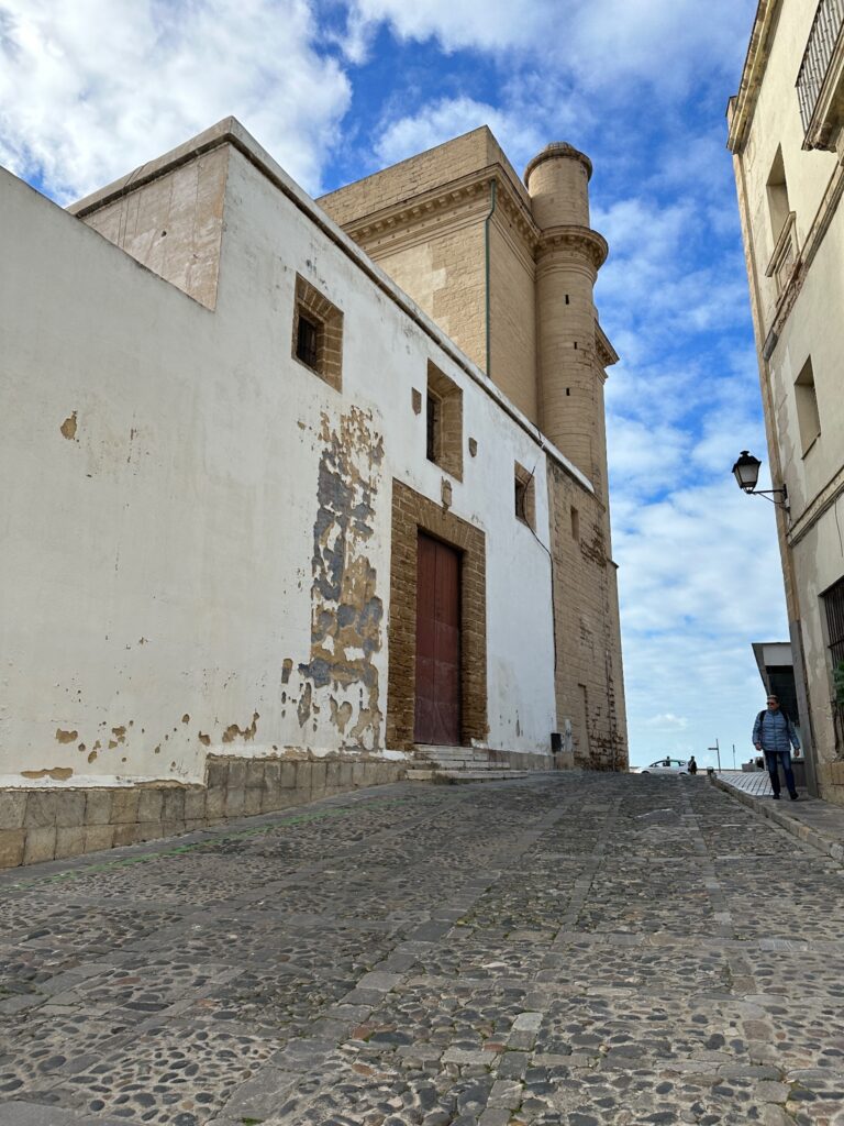 Historic whitewashed building with minaret tower on cobblestone street under blue sky