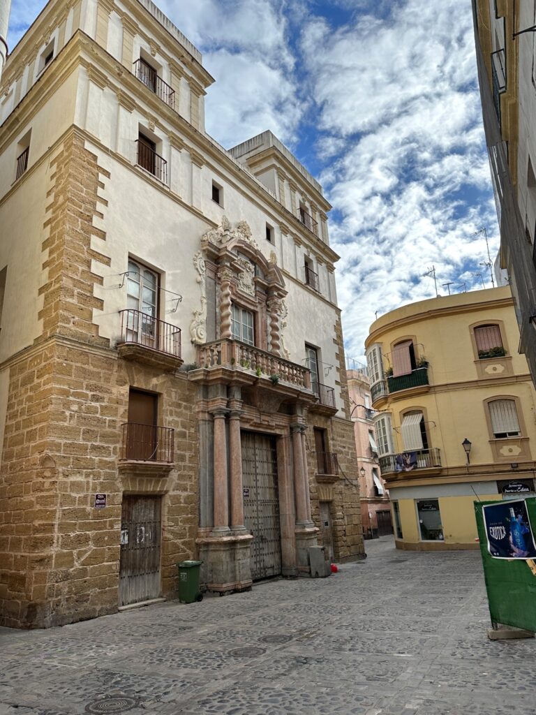 Historic stone palace with ornate baroque entrance in a European plaza under blue sky with clouds