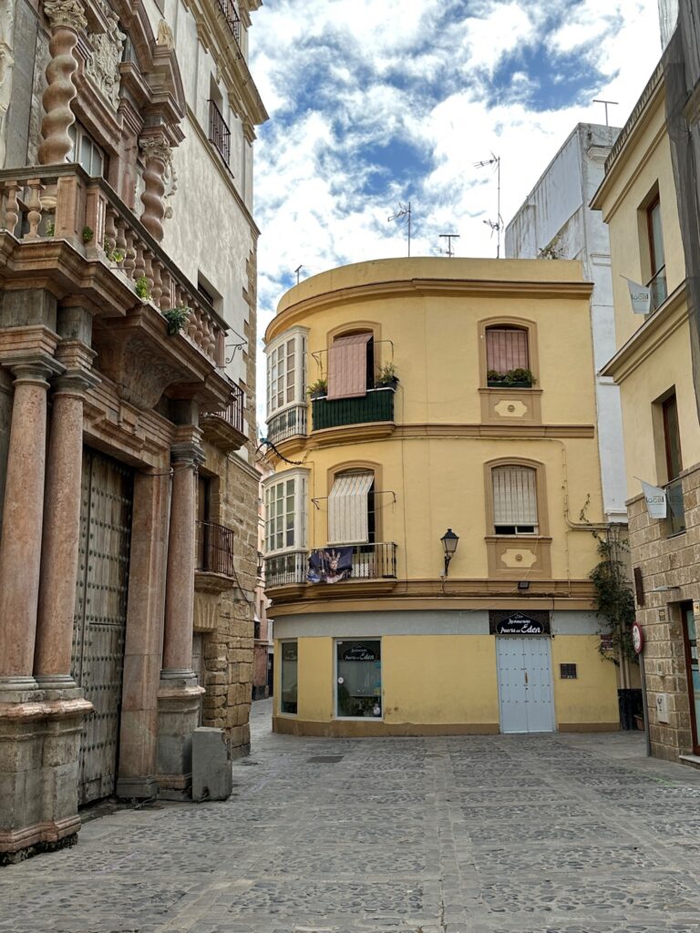 A charming European plaza lined with historic colonial buildings featuring ornate facades, a curved yellow building, and cobblestone streets