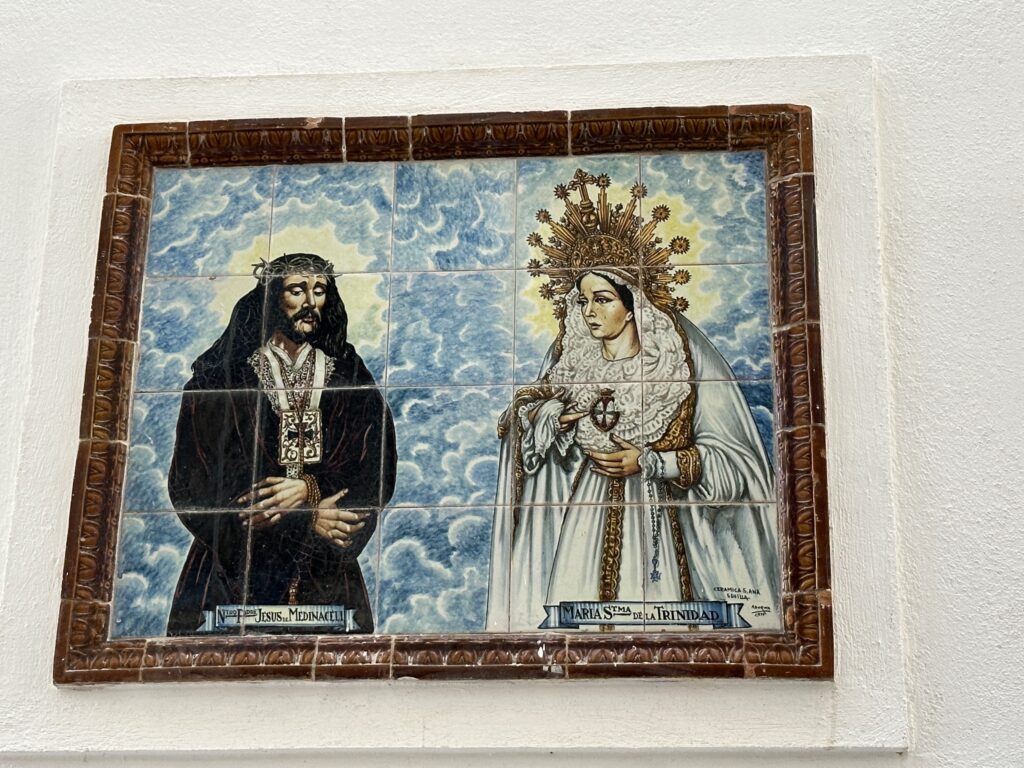 Ceramic tile panel depicting two religious figures with halos against a blue clouded background, framed in ornate brown border