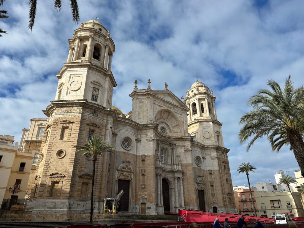 Baroque cathedral with twin domes and bell tower surrounded by palm trees under blue sky in Spanish city