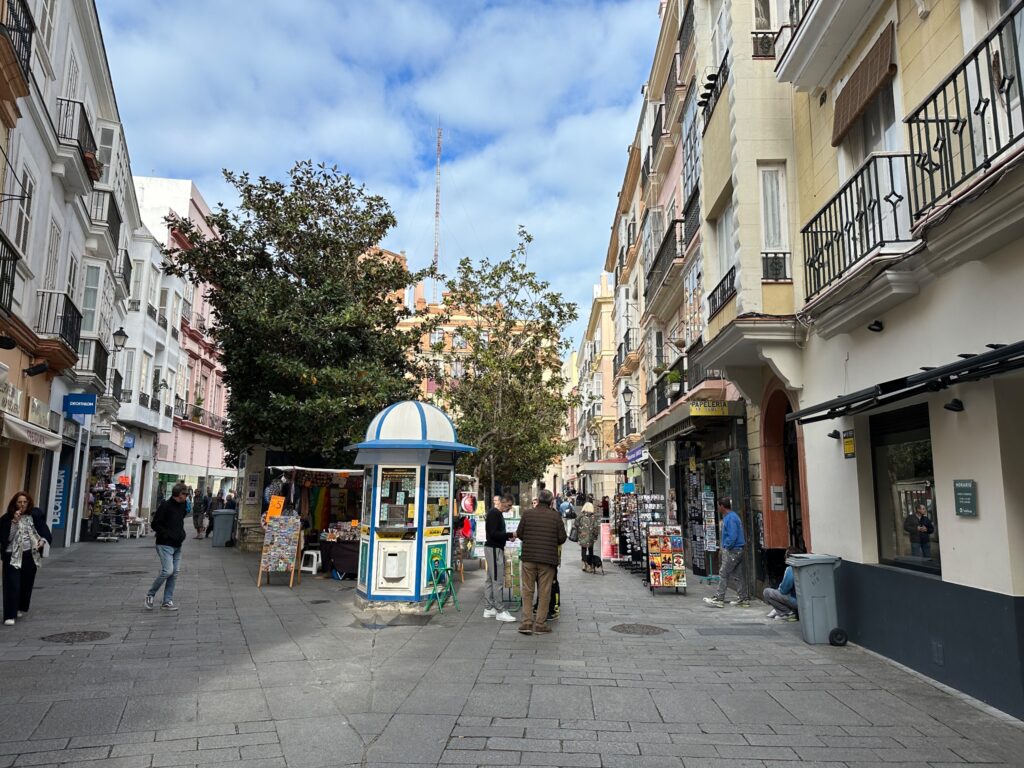 Pedestrian street in a European city with colorful buildings, shops, and a blue-domed kiosk in the center
