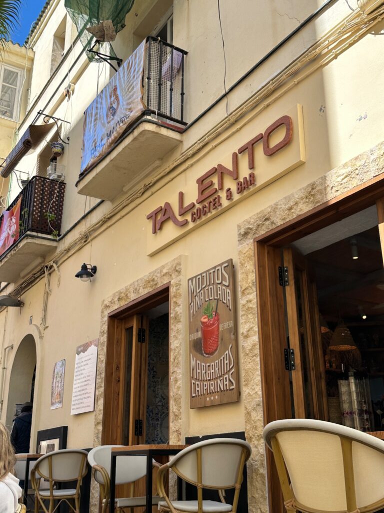 Exterior of Talento tapas bar restaurant with cream-colored facade, wooden doors, and outdoor seating chairs