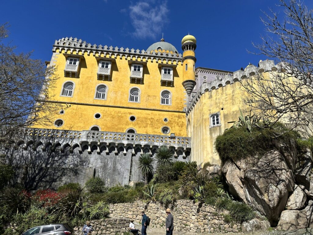 Bright yellow Pena Palace with golden dome towers over lush gardens beneath blue sky in Sintra, Portugal