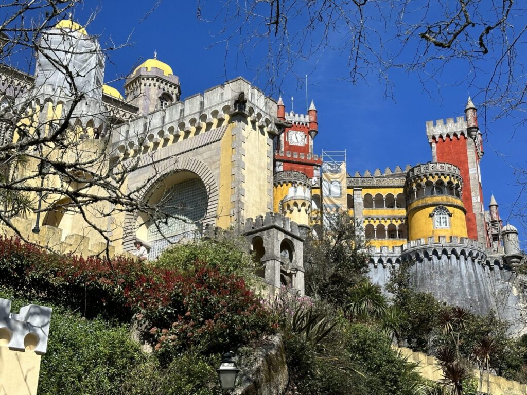Colorful Pena Palace with yellow domes, red towers, and crenellated walls set against blue sky in Sintra