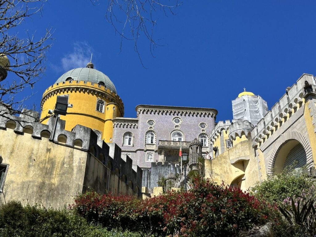 Colorful medieval palace with yellow domed tower and stone walls under bright blue sky in coastal Portugal