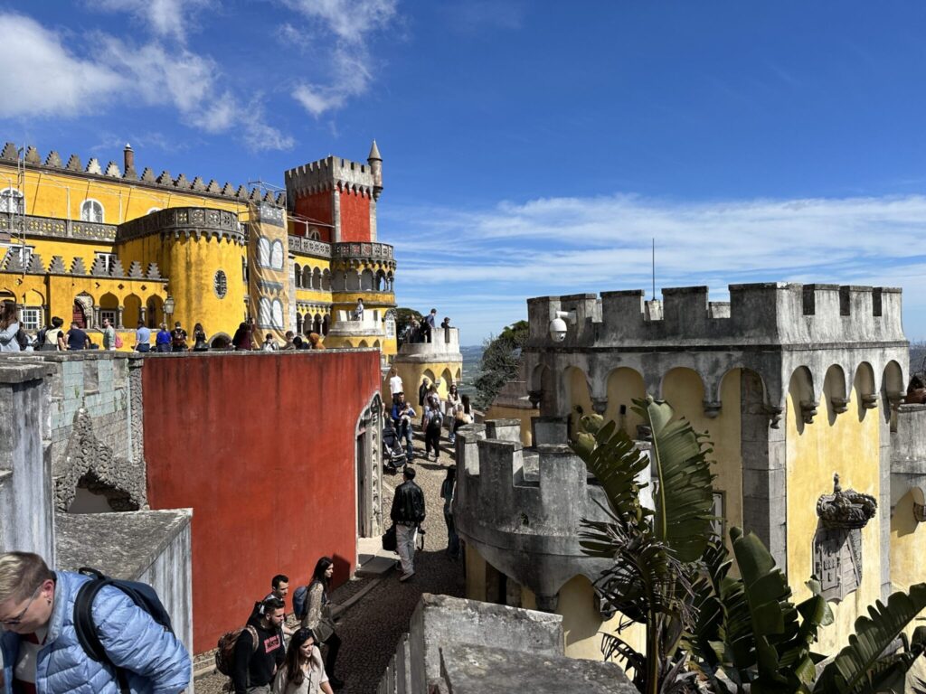 Colorful palaces with crenellated towers and tourists exploring the historic hilltop fortress of Pena Palace in Sintra, Portugal