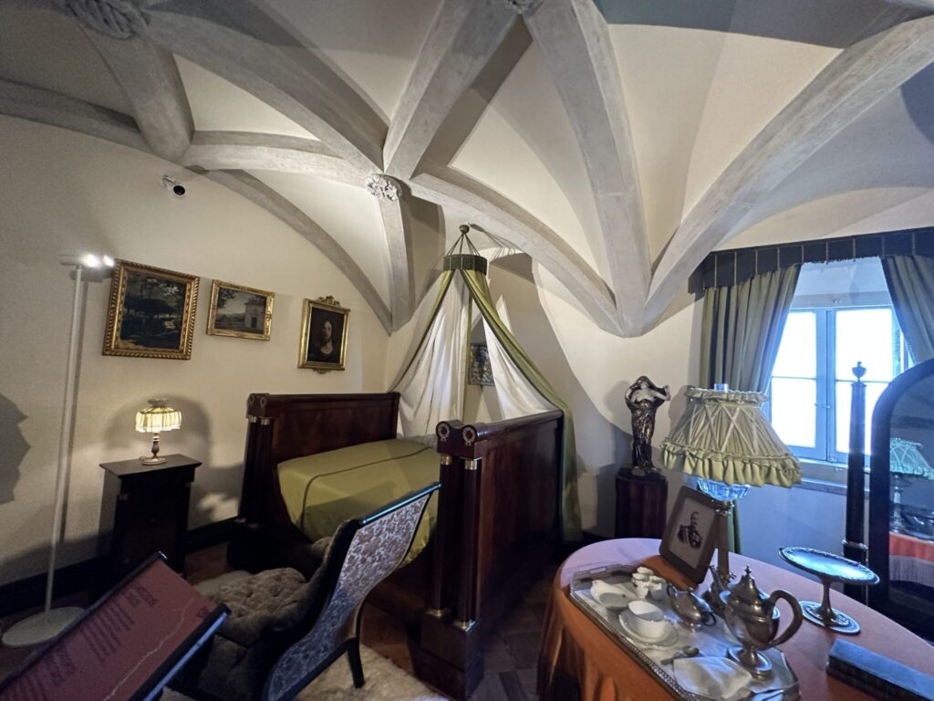 Historic bedroom with canopy bed, period furniture, artwork, and ornate ceiling beams in a museum or heritage setting